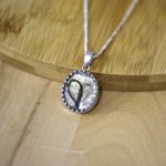 Ovaler Silberanhänger an feiner Kette, im Inneren ein Herz aus Haar, auf hellem Holz.