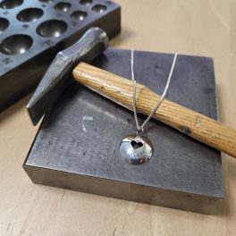 Handgefertigter Silberanhänger und Goldschmiedehammer in einer Werkstatt in Liestal.